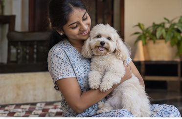A woman holds a small dog close while seated indoors.