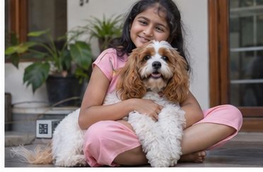 A young girl sitting with a small fluffy brown-and-white dog on a tiled porch