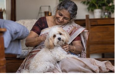 A woman seated beside a sofa pets a small white dog.