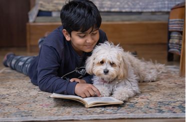 A child sits cross-legged beside a small dog resting on a rug.