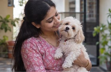 A woman cradles a small white dog while sitting on a rug.
