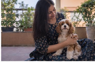 A woman sits outdoors with a small brown-and-white dog on her lap