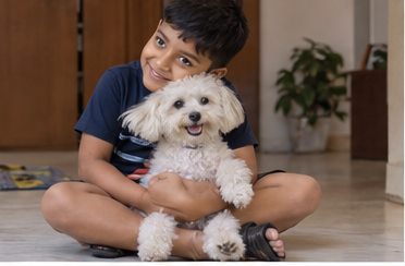 A man sits cross-legged and holds a small white dog.