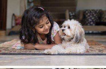 A child writes at a low table beside a small white dog.
