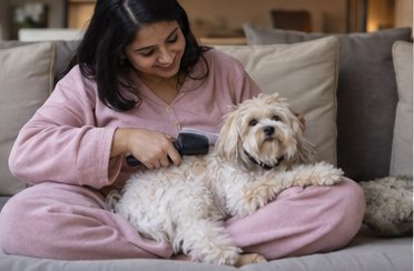 A woman sits on the floor and pets a small dog.