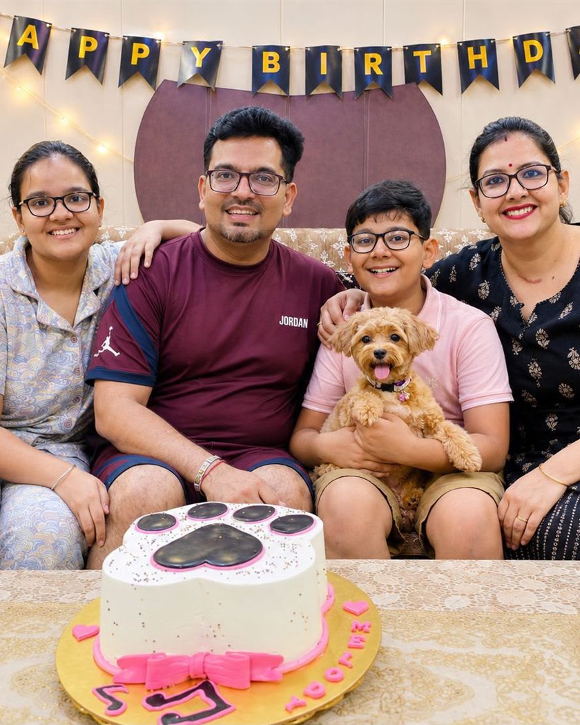 Family of four sitting together at a birthday celebration with their apricot curly-coated dog and a paw-print cake